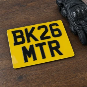 Yellow two-line motorcycle number plate reading BK26 MTR next to a glove